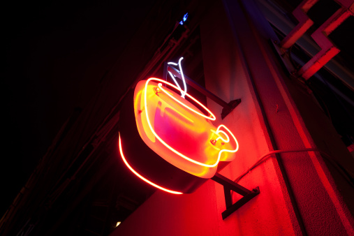 A bright neon cup of coffee sign on the side of a building